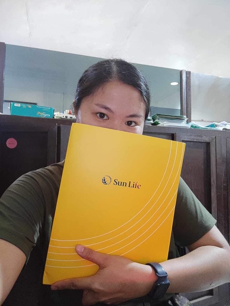 A client at her shop counter, holding her Sun Life policy folder up to her face